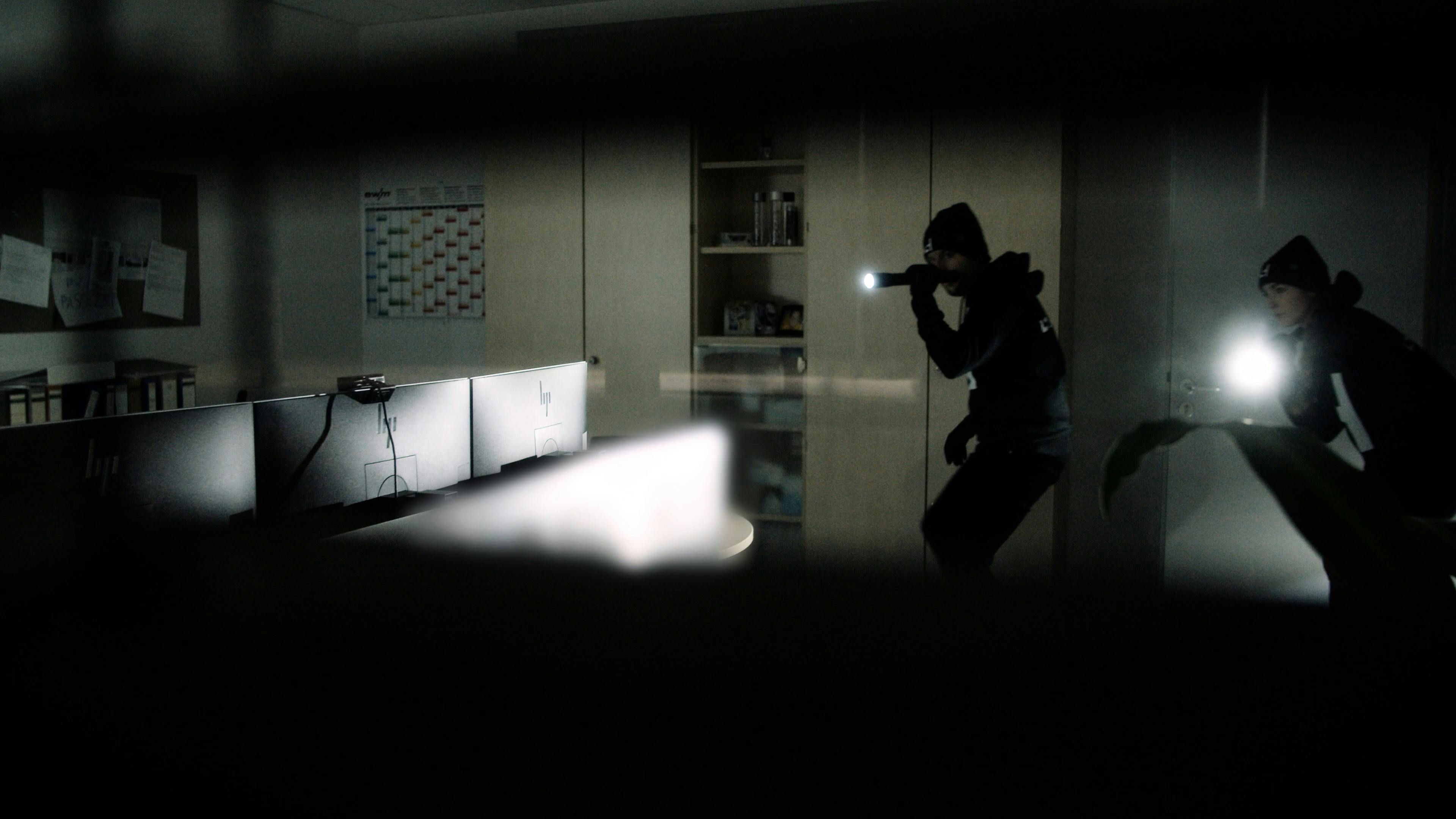 Zwei Einbrecher leuchten mit Taschenlampen durch ein dunkles Büro
