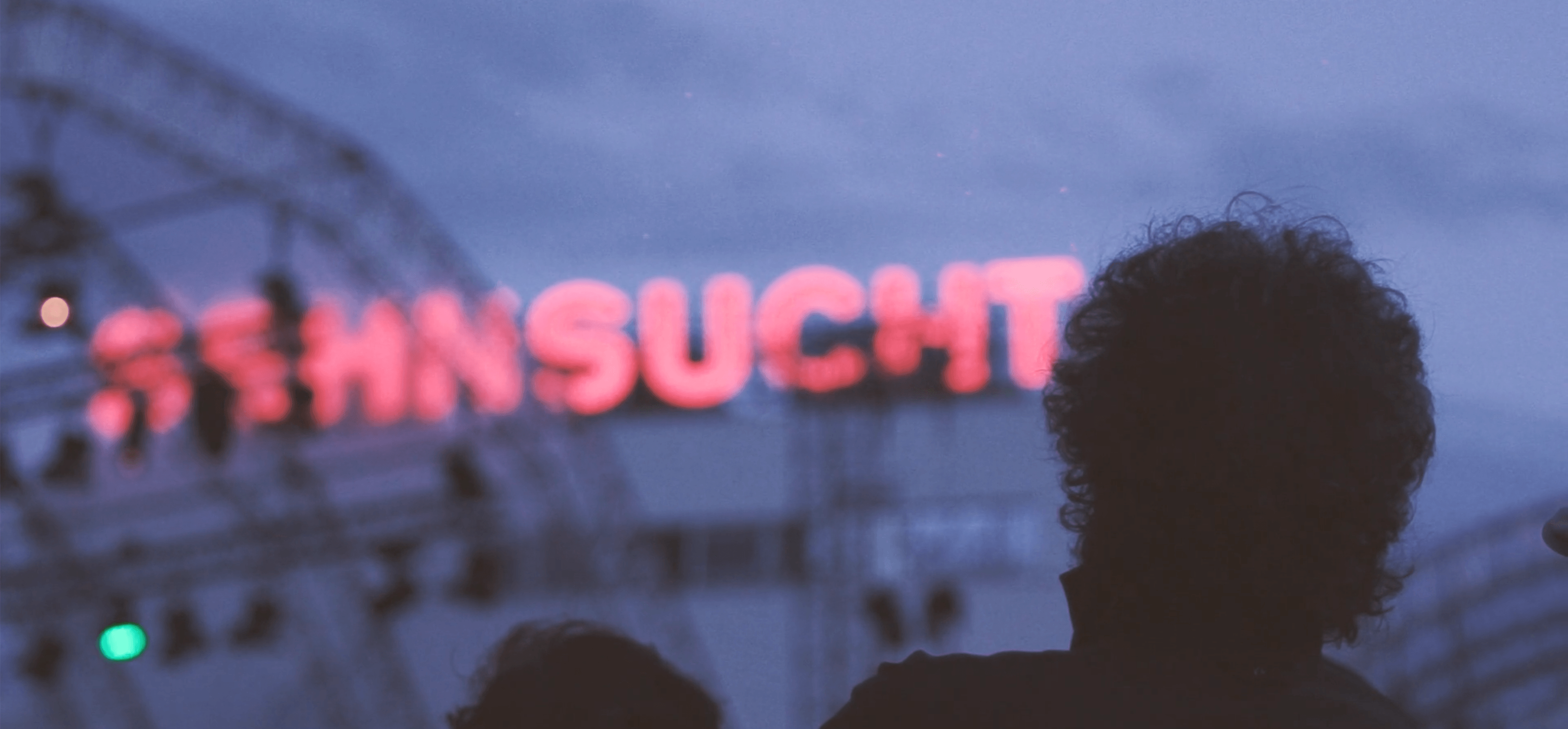 Abenddämmerung mit Kopf im Vordergrund und dem rot leuchtenden Schriftzug Sehnsucht im Hintergrund