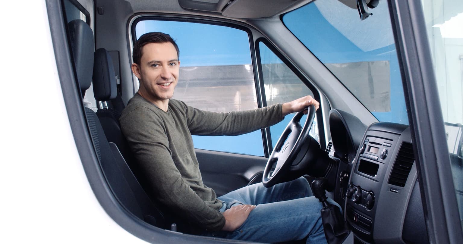 Der Fahrer eines LKWs lächelt durch das Seitenfenster in die Kamera