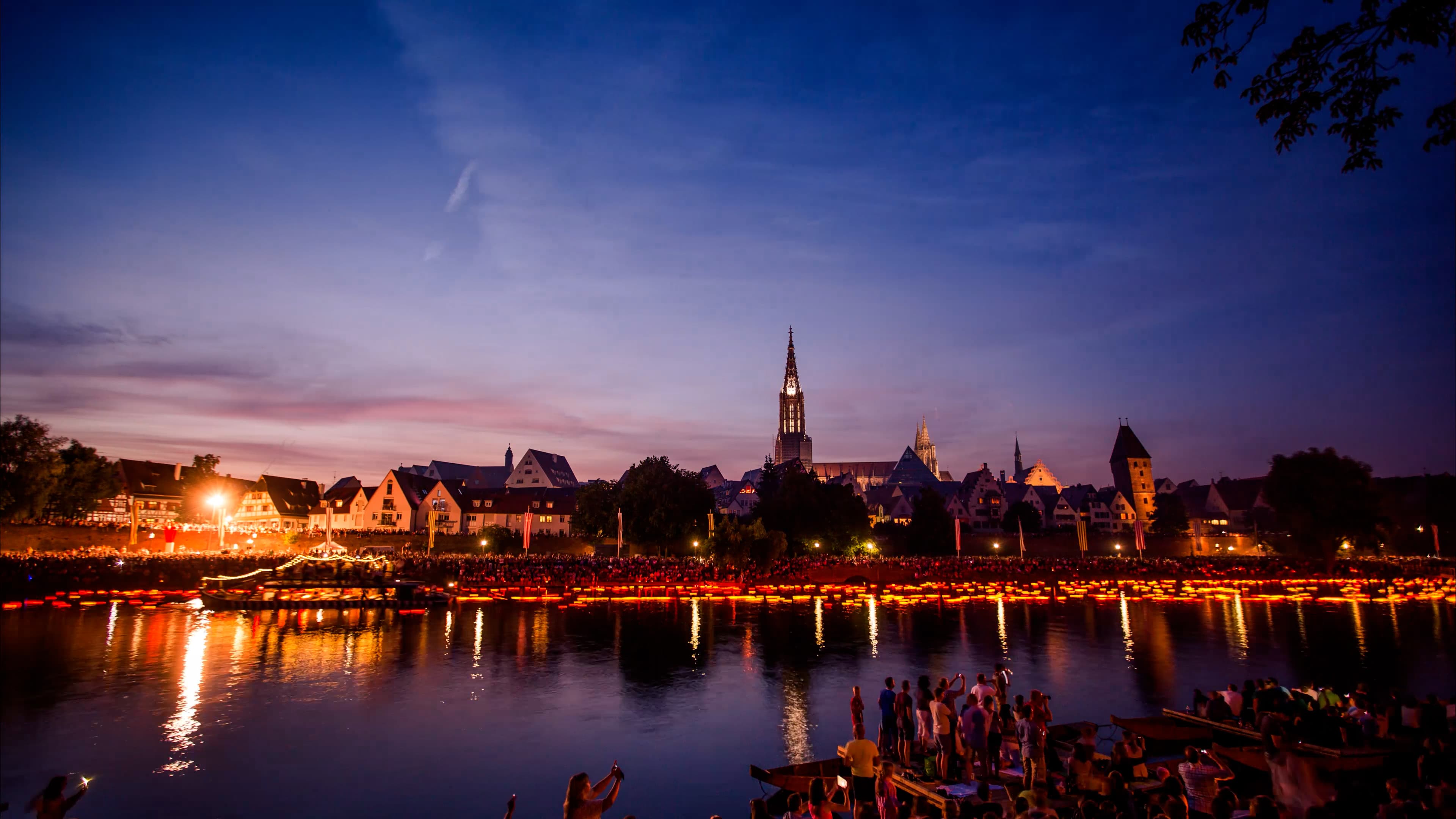 Lichterserenade in Ulm, in der Abenddämmerung schwimmen hunderte Lichter auf der Donau vor der Kulisse des Ulmer Donauufers