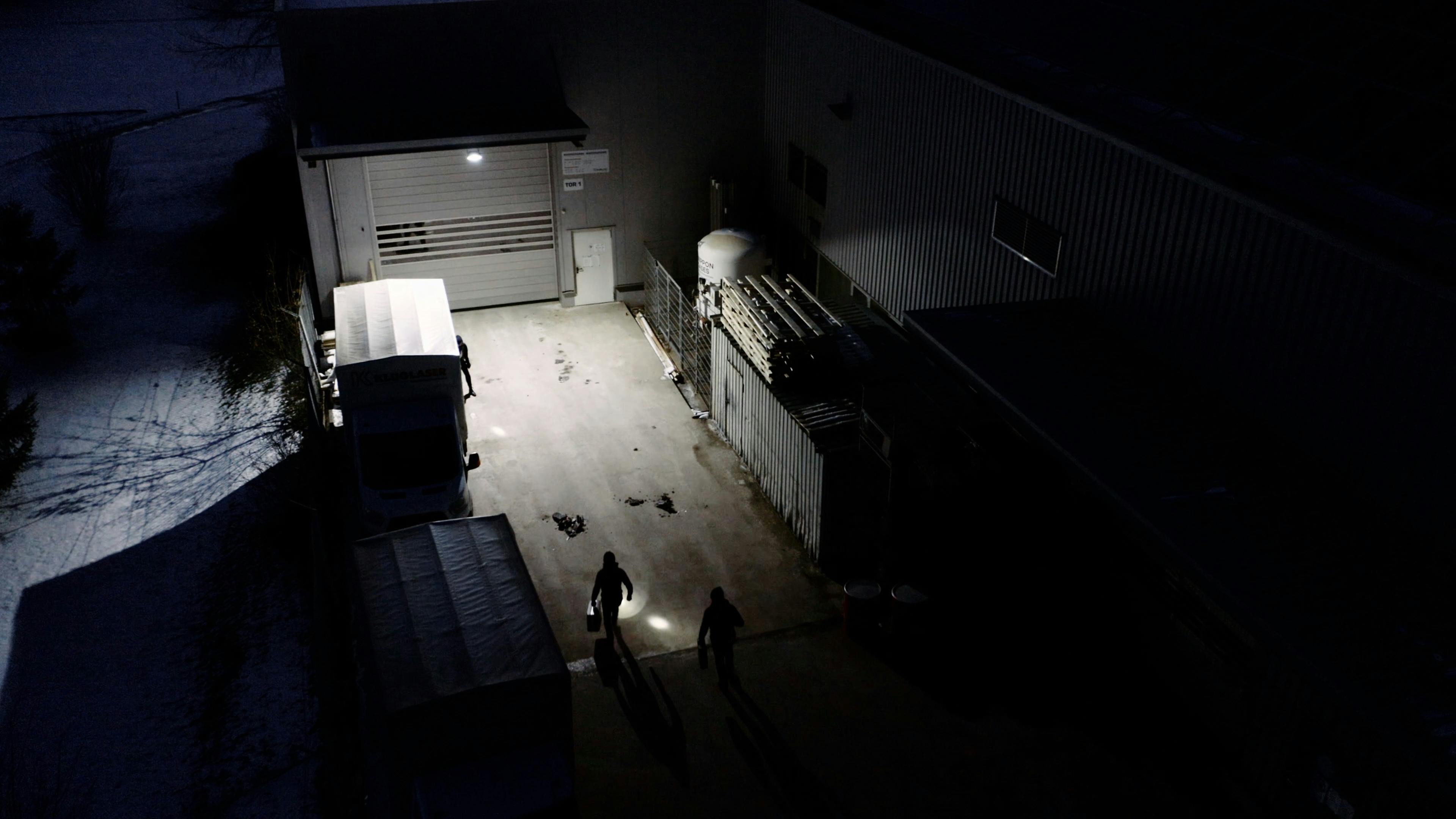 Drei Einbrecher mit Taschenlampen auf dem Weg zu einer Tür einer Fabrik aus Vogelperspektive