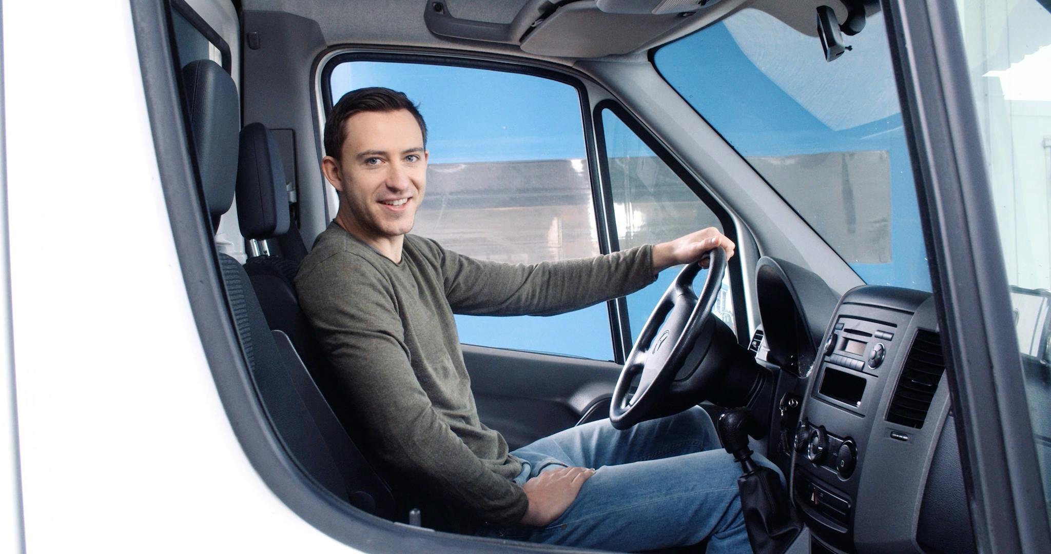Der Fahrer eines LKWs lächelt durch das Seitenfenster in die Kamera