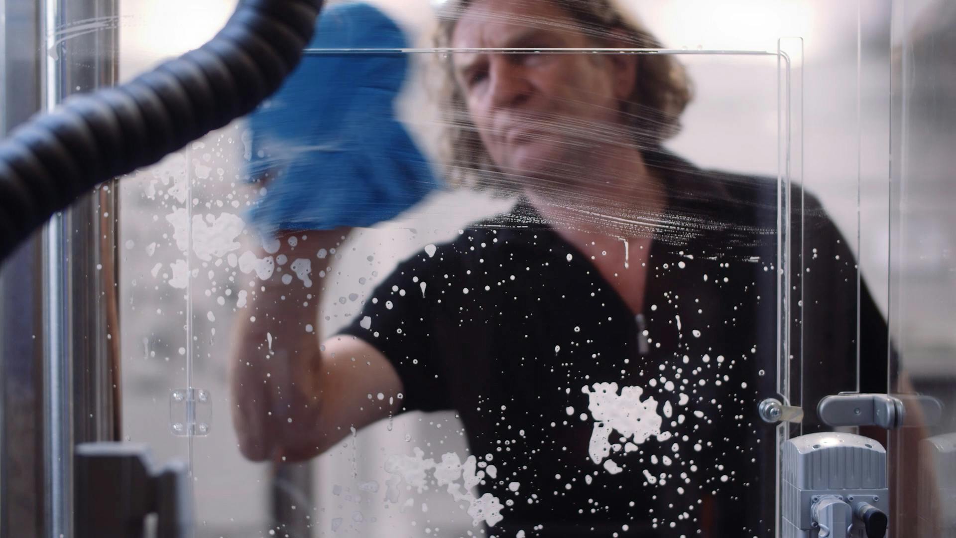 Ein Mitarbeiter von Festo reinigt die Plexiglasscheibe eines Messestand-Exponats mit Reinigungsmittel und Putzlappen